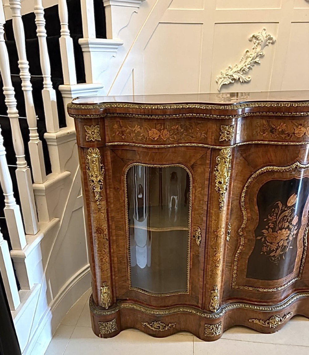 A Victorian serpentine burr walnut credenza featuring detailed floral marquetry inlays, gilt-bronze mounts, a central panelled door, and two curved glazed side doors. View XV