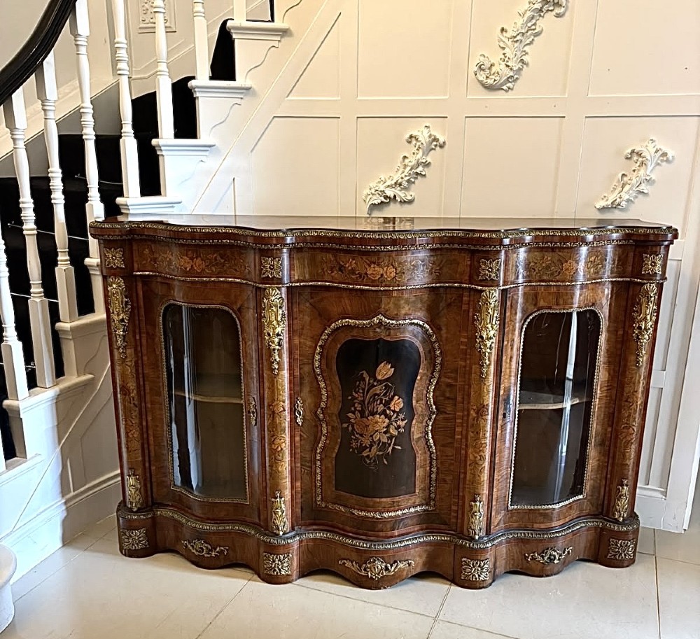 A Victorian serpentine burr walnut credenza featuring detailed floral marquetry inlays, gilt-bronze mounts, a central panelled door, and two curved glazed side doors.
