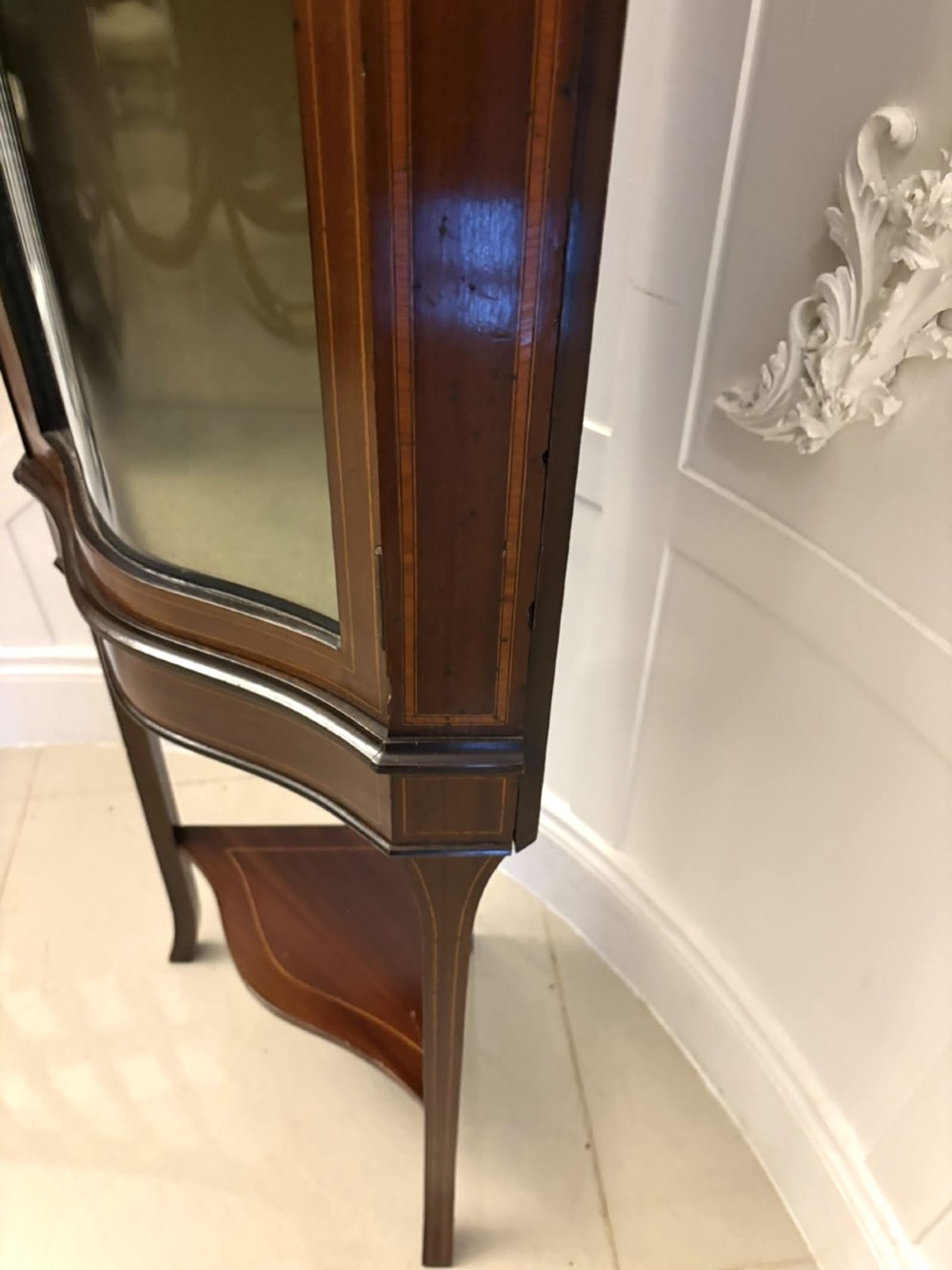 An Edwardian mahogany corner display cabinet with a serpentine glazed door, line inlay decoration, shaped upper pediment, and slender tapered legs with a lower undertier. View III