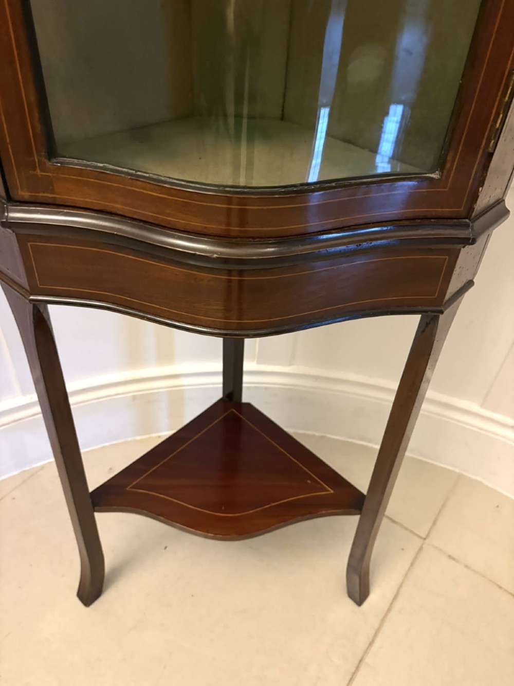 An Edwardian mahogany corner display cabinet with a serpentine glazed door, line inlay decoration, shaped upper pediment, and slender tapered legs with a lower undertier. View VIII