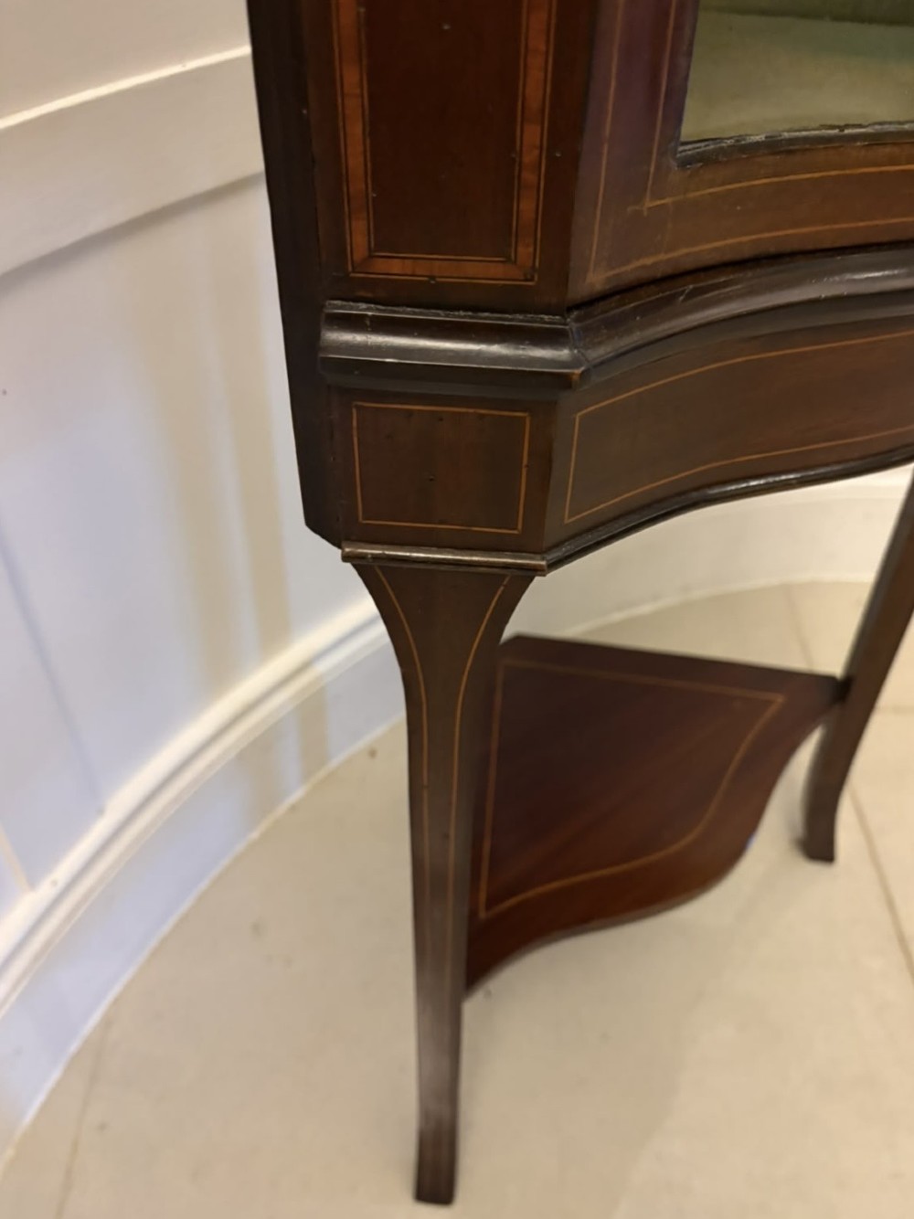 An Edwardian mahogany corner display cabinet with a serpentine glazed door, line inlay decoration, shaped upper pediment, and slender tapered legs with a lower undertier. View IX