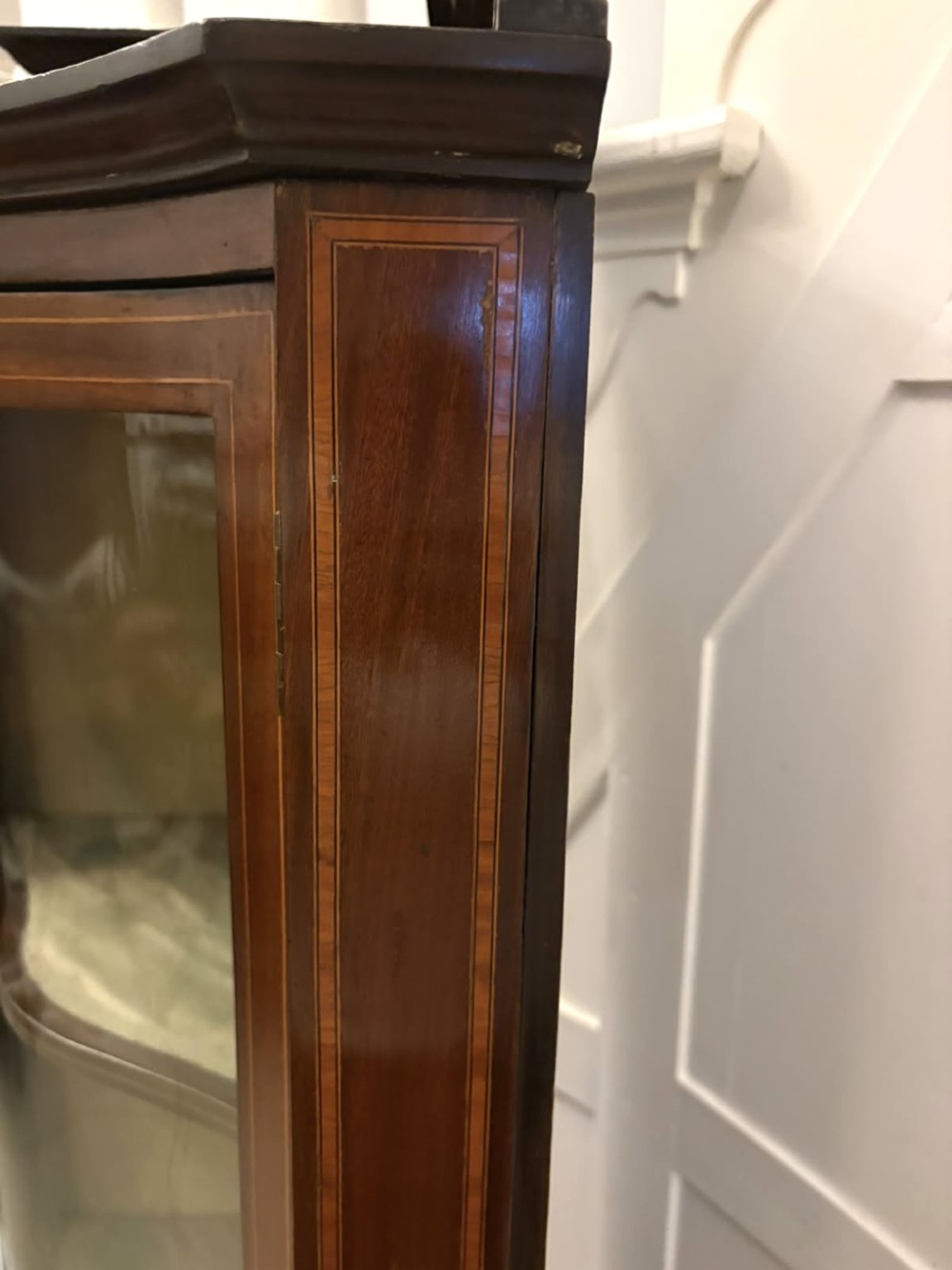 An Edwardian mahogany corner display cabinet with a serpentine glazed door, line inlay decoration, shaped upper pediment, and slender tapered legs with a lower undertier. View X