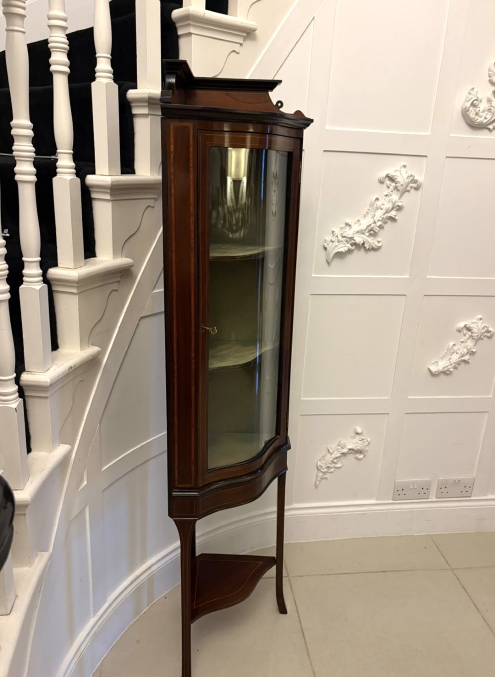 An Edwardian mahogany corner display cabinet with a serpentine glazed door, line inlay decoration, shaped upper pediment, and slender tapered legs with a lower undertier. View XI