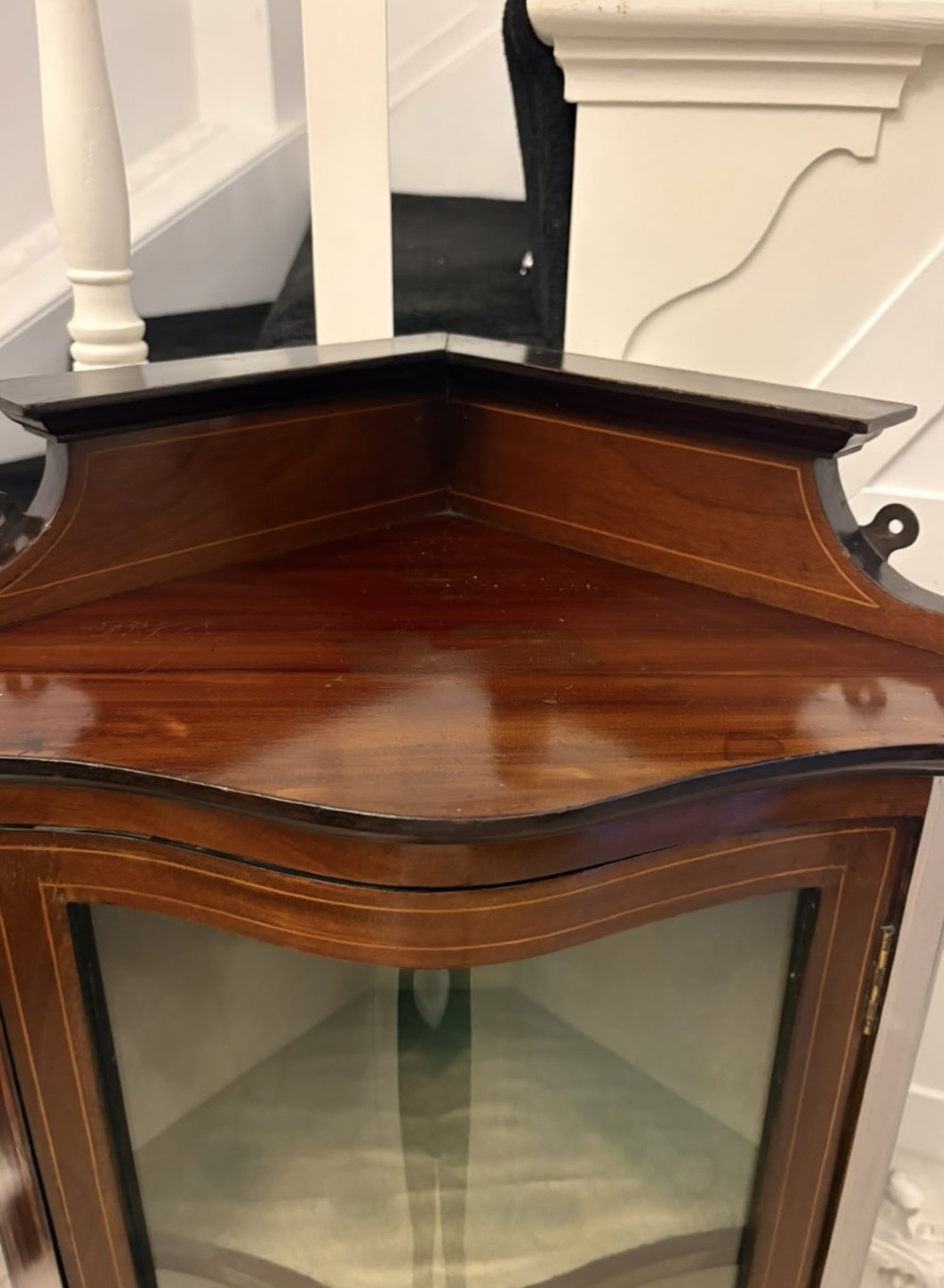 An Edwardian mahogany corner display cabinet with a serpentine glazed door, line inlay decoration, shaped upper pediment, and slender tapered legs with a lower undertier. View XII