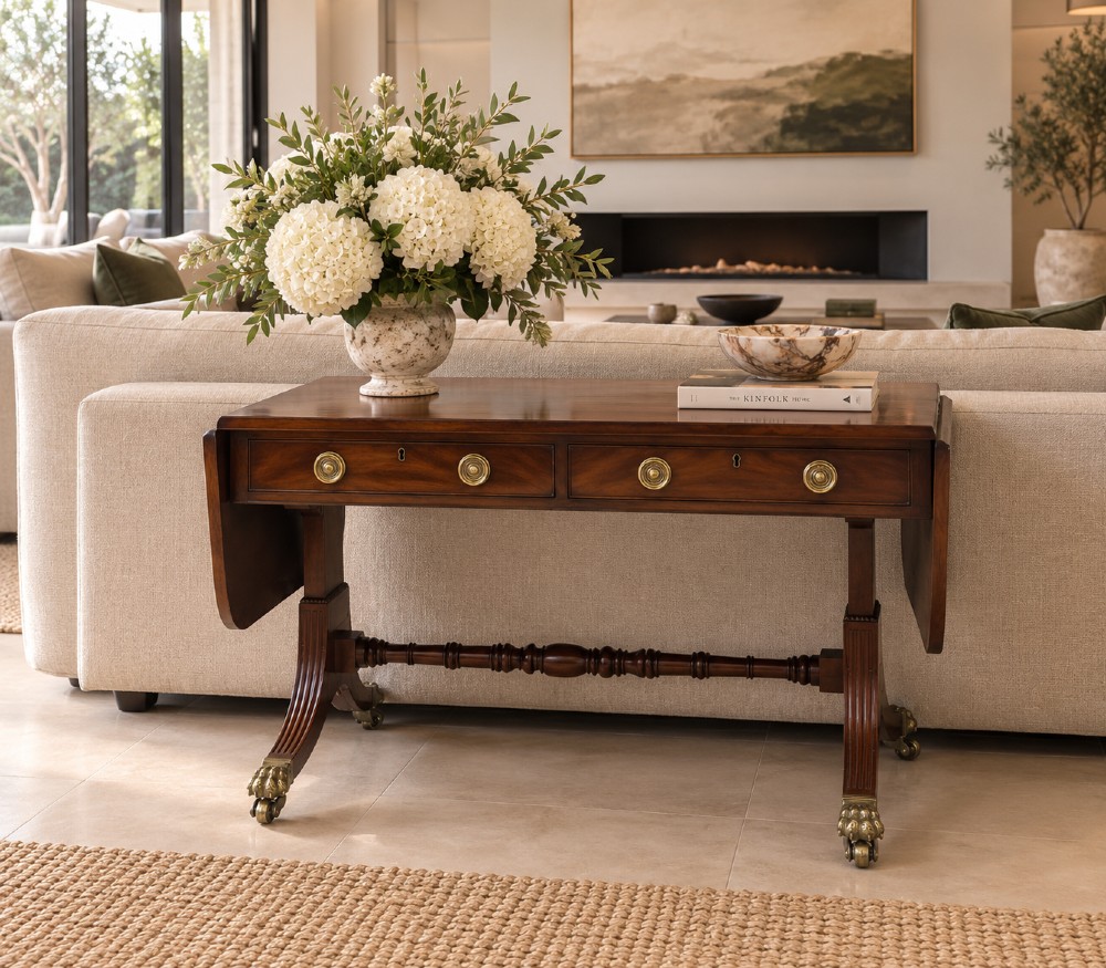 A Regency mahogany sofa table featuring two drop leaves, two front drawers with round brass knobs, reeded splayed legs, and brass paw castors. View II