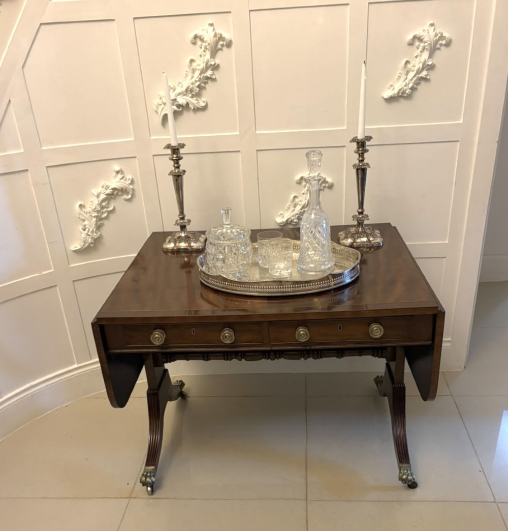 A Regency mahogany sofa table featuring two drop leaves, two front drawers with round brass knobs, reeded splayed legs, and brass paw castors. View IV