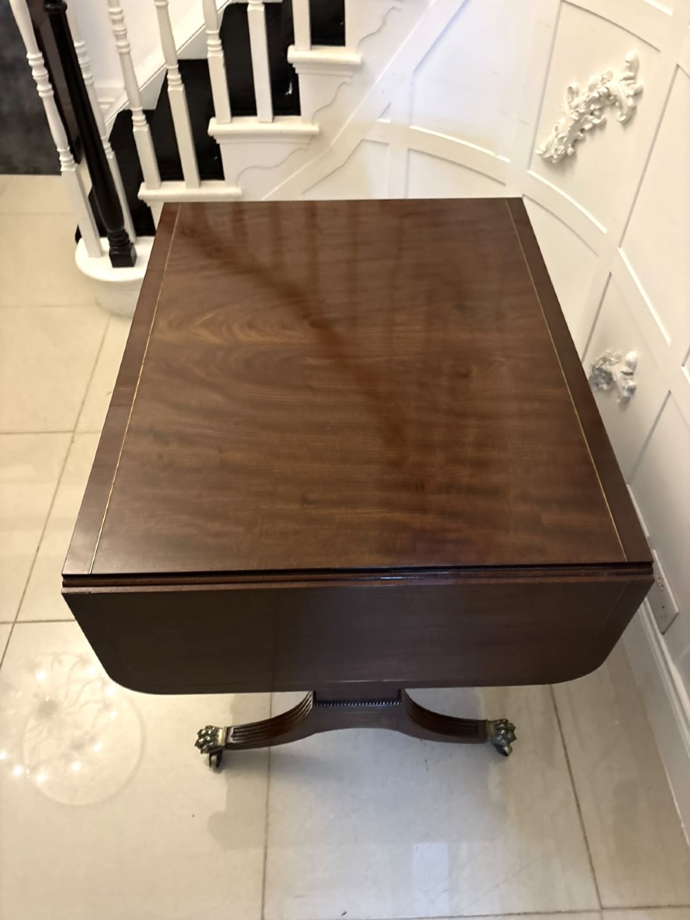 A Regency mahogany sofa table featuring two drop leaves, two front drawers with round brass knobs, reeded splayed legs, and brass paw castors. View XI