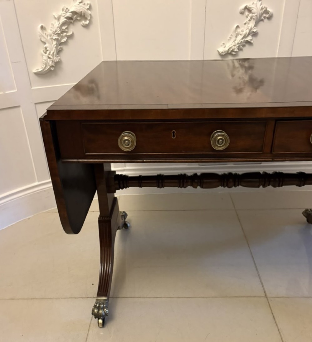 A Regency mahogany sofa table featuring two drop leaves, two front drawers with round brass knobs, reeded splayed legs, and brass paw castors. View XII