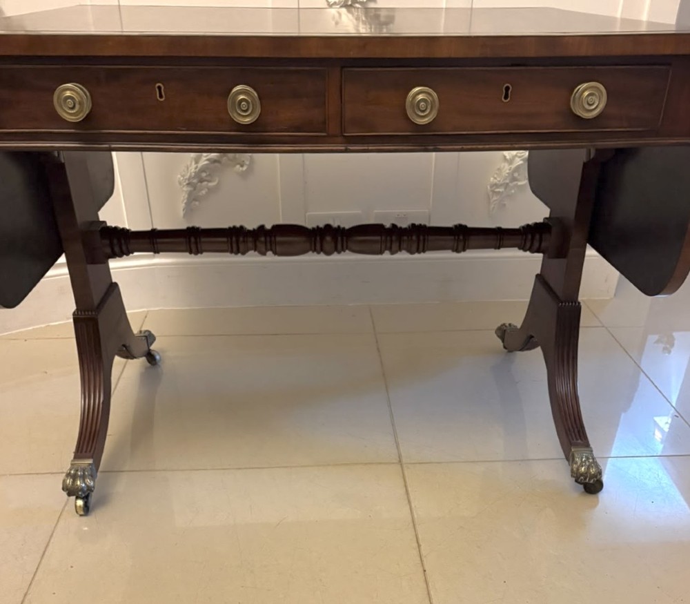 A Regency mahogany sofa table featuring two drop leaves, two front drawers with round brass knobs, reeded splayed legs, and brass paw castors. View XIV