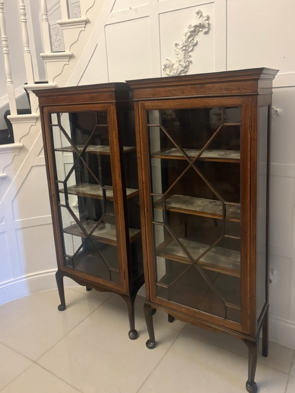 A pair of tall Edwardian mahogany display cabinets with geometric astragal glazed glass doors and slender cabriole legs. View XV