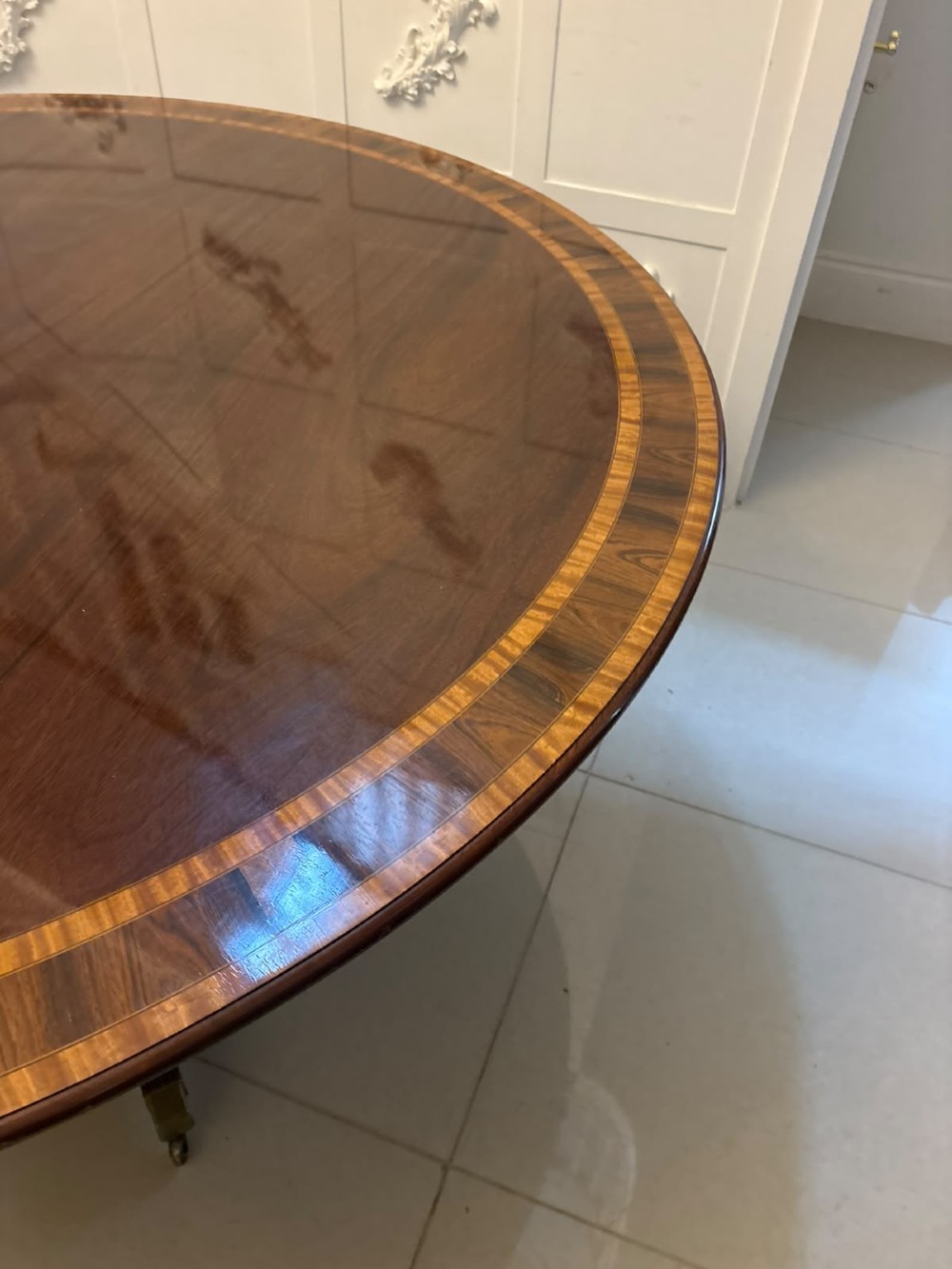 A large circular mahogany dining table featuring rosewood and satinwood crossbanding set upon a central pedestal base with reeded legs ending in brass castors. View III