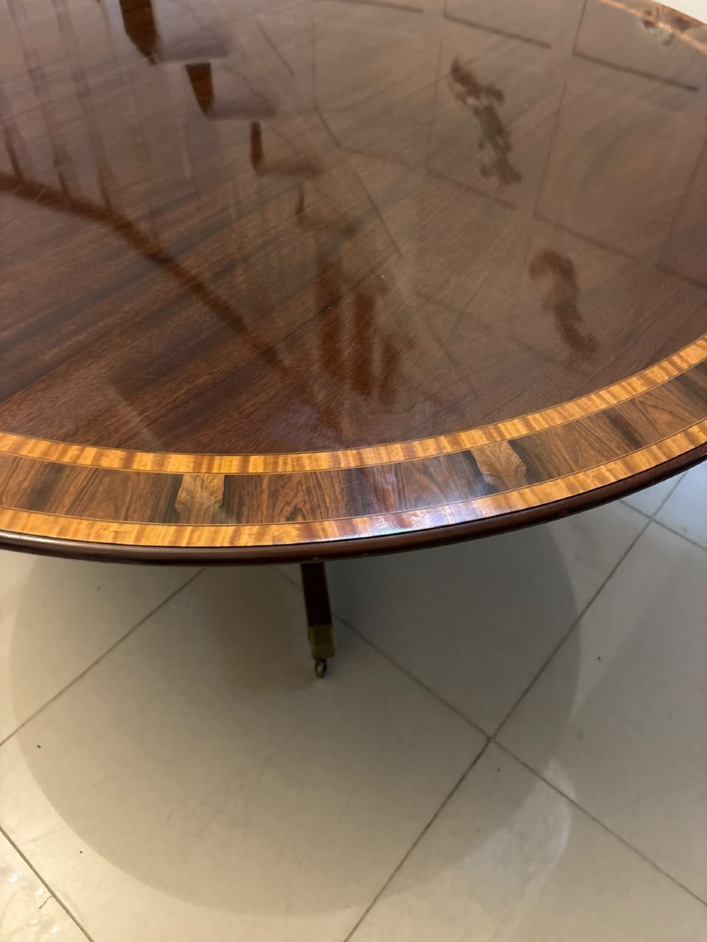 A large circular mahogany dining table featuring rosewood and satinwood crossbanding set upon a central pedestal base with reeded legs ending in brass castors. View VI