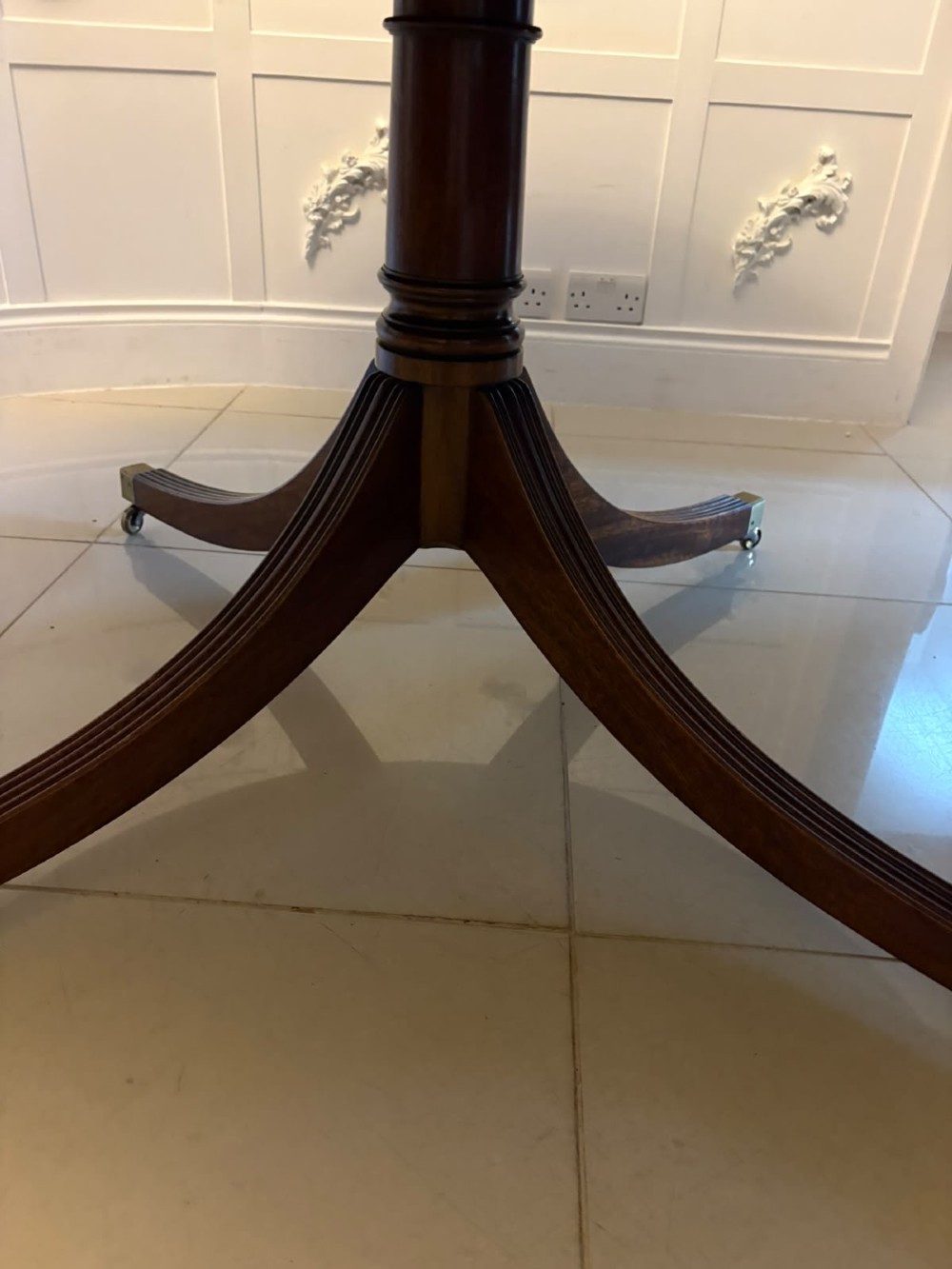 A large circular mahogany dining table featuring rosewood and satinwood crossbanding set upon a central pedestal base with reeded legs ending in brass castors. View VII
