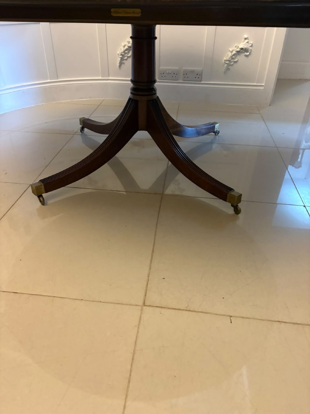 A large circular mahogany dining table featuring rosewood and satinwood crossbanding set upon a central pedestal base with reeded legs ending in brass castors. View IX