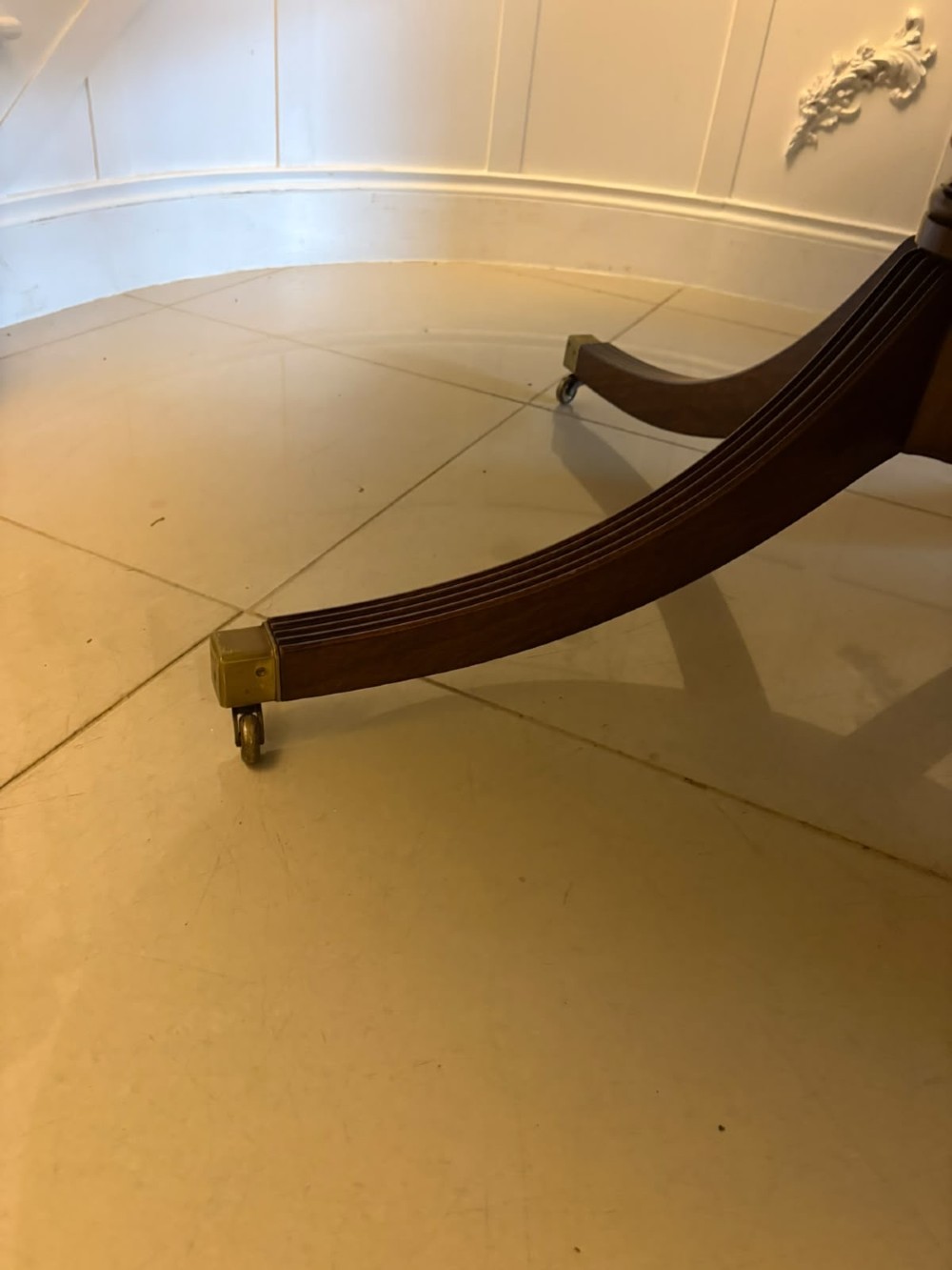 A large circular mahogany dining table featuring rosewood and satinwood crossbanding set upon a central pedestal base with reeded legs ending in brass castors. View X