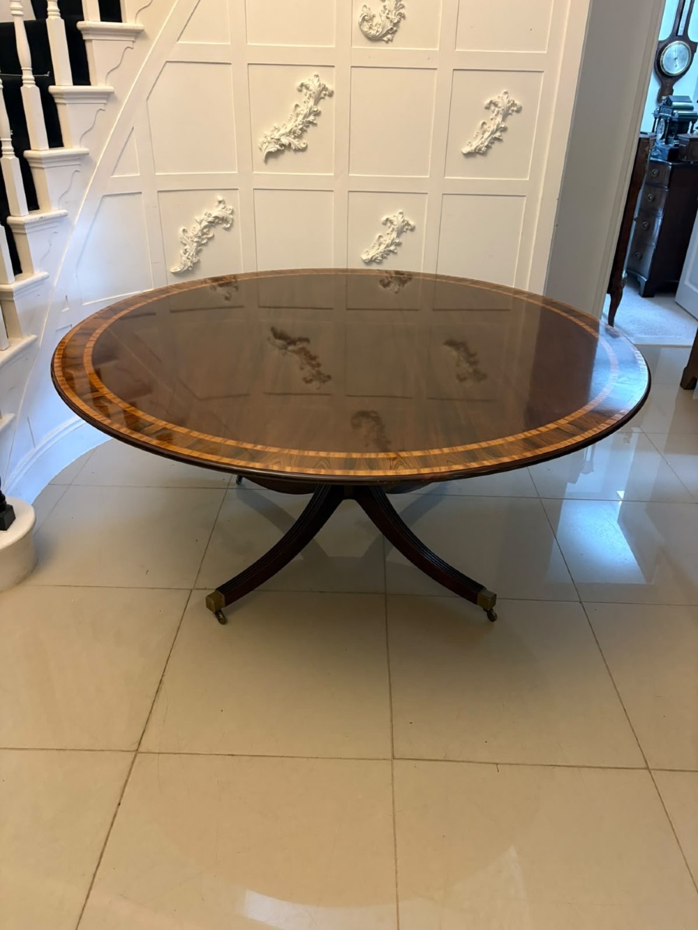A large circular mahogany dining table featuring rosewood and satinwood crossbanding set upon a central pedestal base with reeded legs ending in brass castors. View XI
