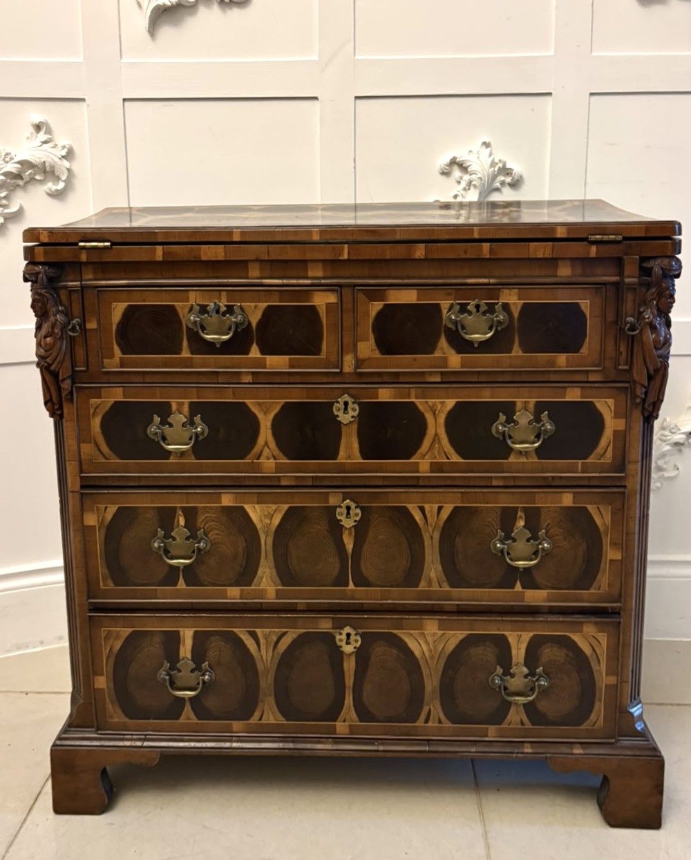 A George I yew wood and laburnum oyster veneered bachelors chest of drawers with carved corner caryatids and brass drop handles.