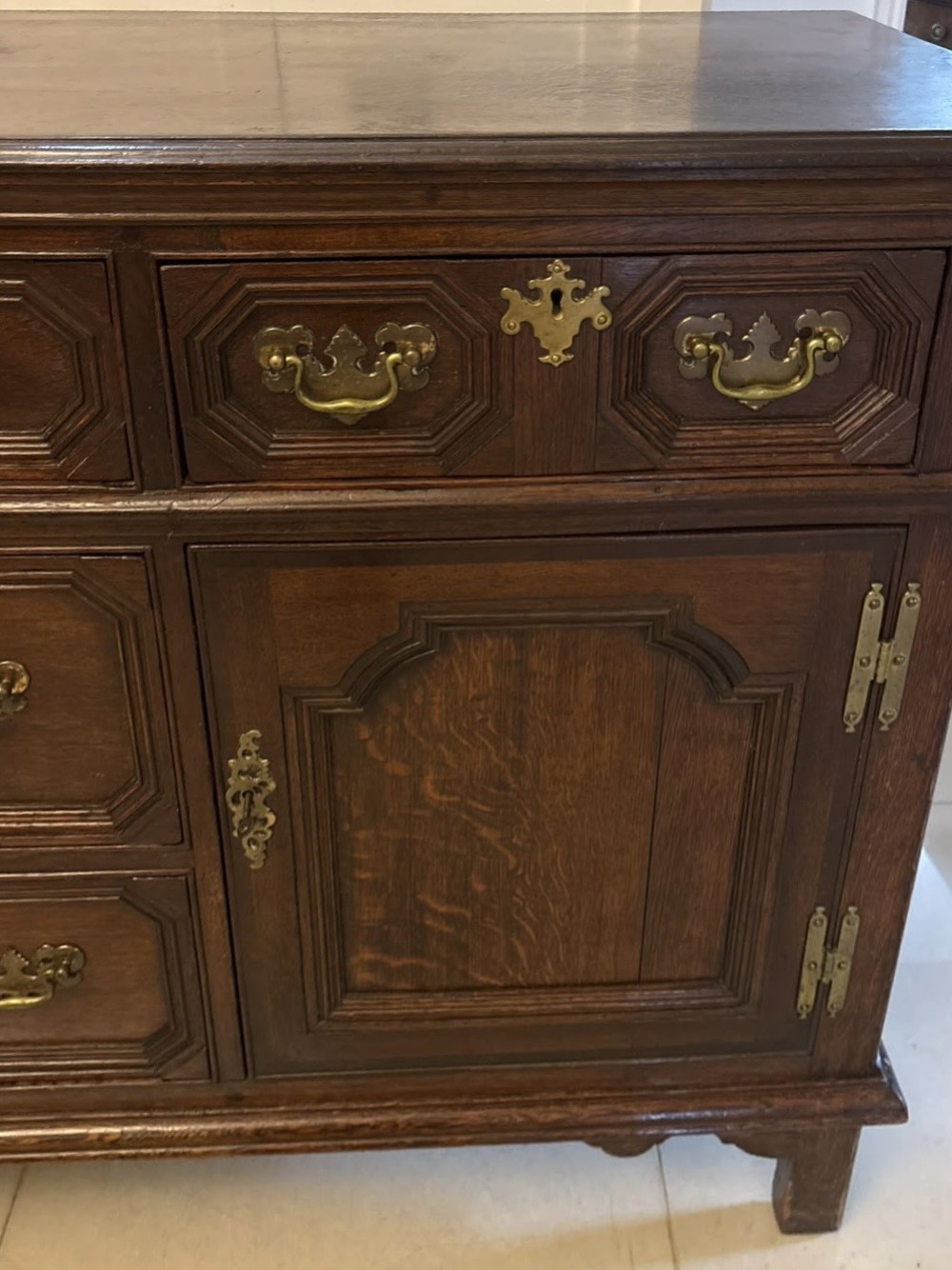 An antique dark oak Georgian dresser base featuring geometric panel drawers, brass handles, side cupboard doors, and a smooth wooden surface. View V