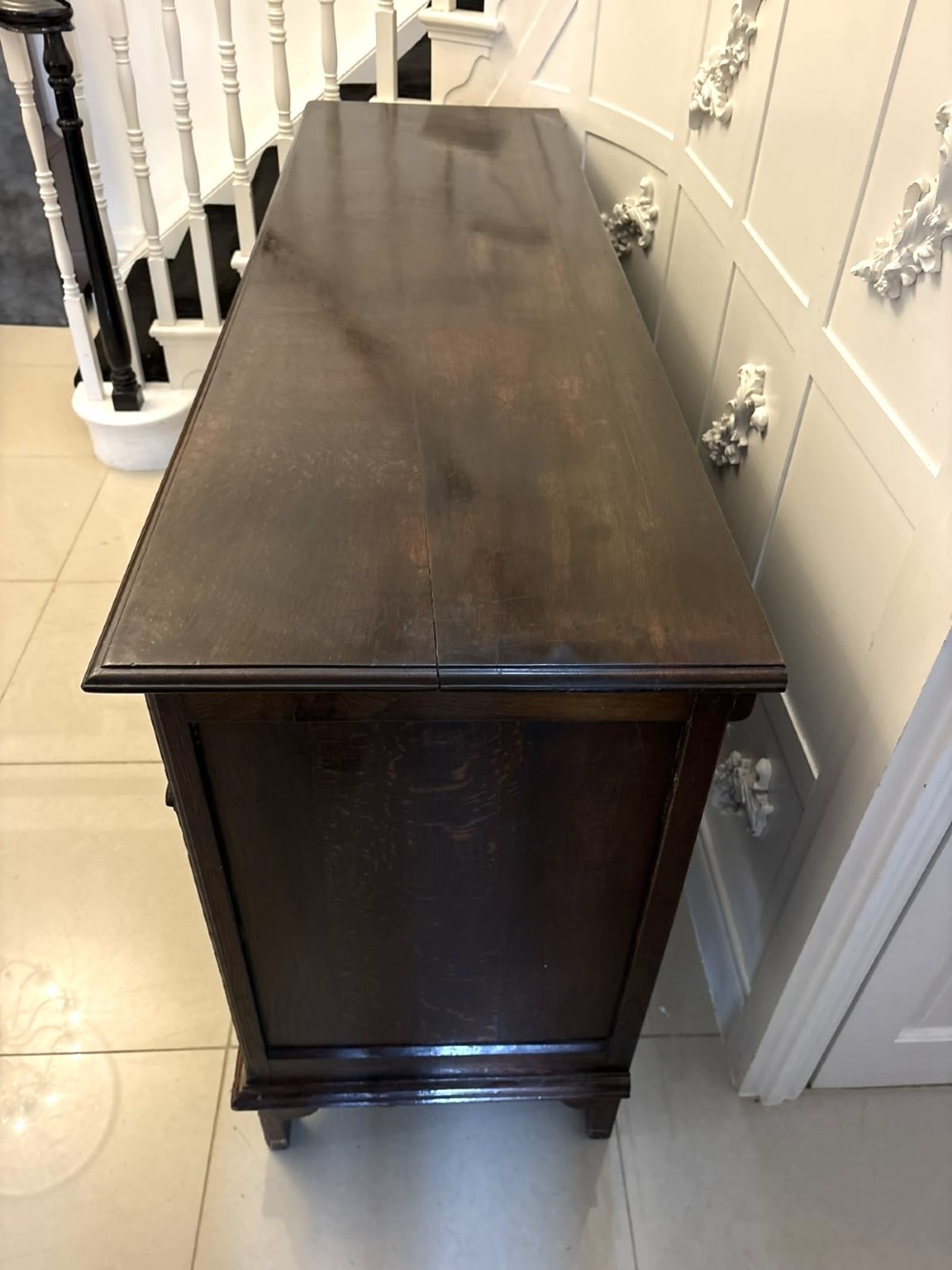 An antique dark oak Georgian dresser base featuring geometric panel drawers, brass handles, side cupboard doors, and a smooth wooden surface. View VII