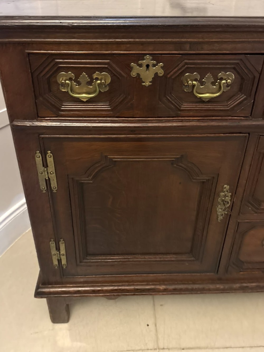 An antique dark oak Georgian dresser base featuring geometric panel drawers, brass handles, side cupboard doors, and a smooth wooden surface. View IX