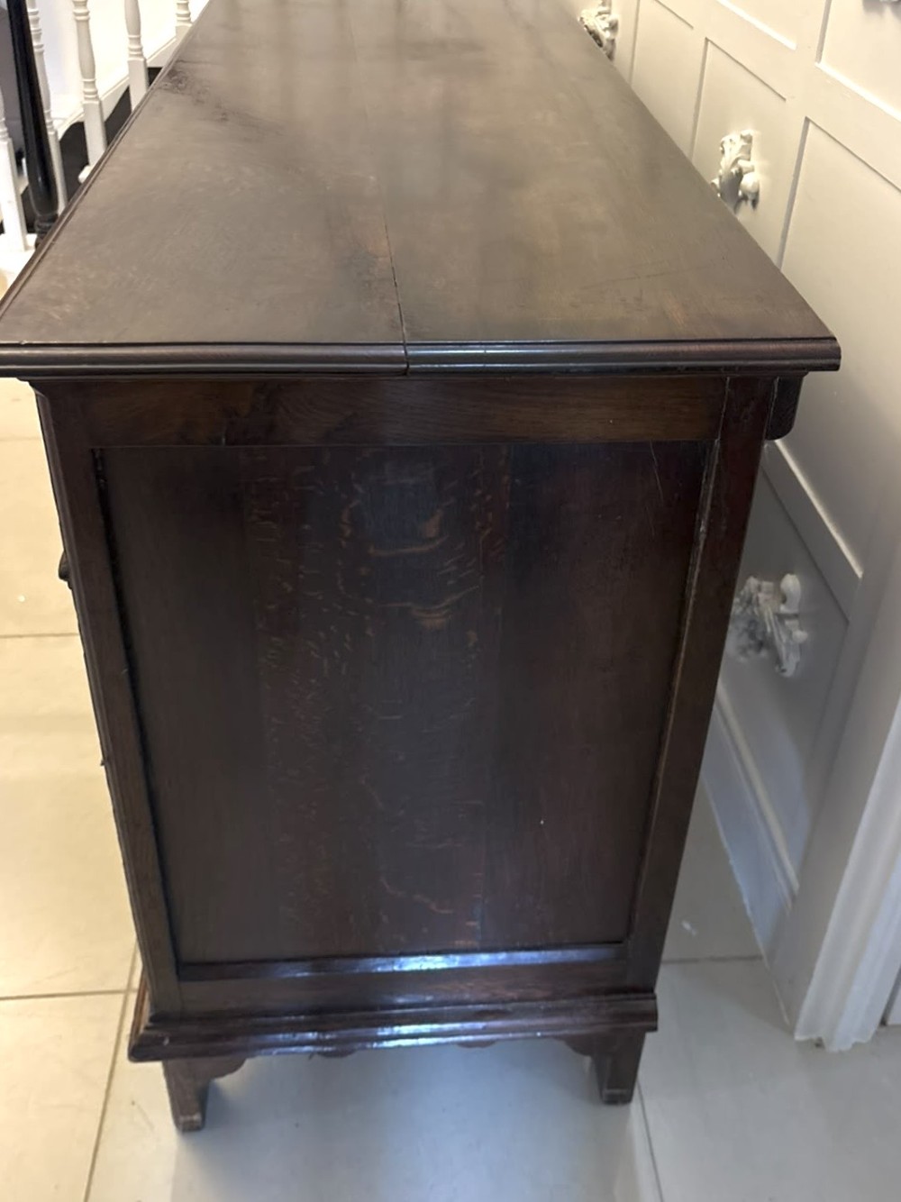 An antique dark oak Georgian dresser base featuring geometric panel drawers, brass handles, side cupboard doors, and a smooth wooden surface. View X