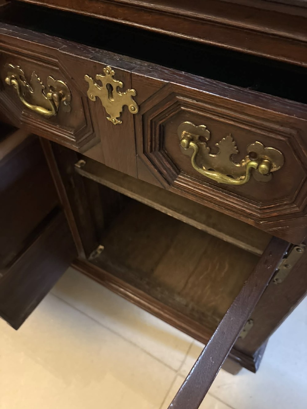 An antique dark oak Georgian dresser base featuring geometric panel drawers, brass handles, side cupboard doors, and a smooth wooden surface. View XI