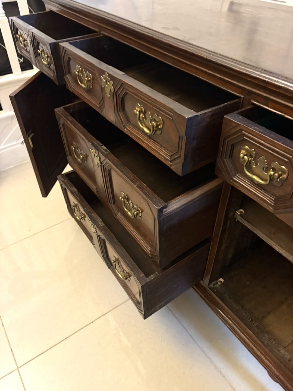 An antique dark oak Georgian dresser base featuring geometric panel drawers, brass handles, side cupboard doors, and a smooth wooden surface. View XIII