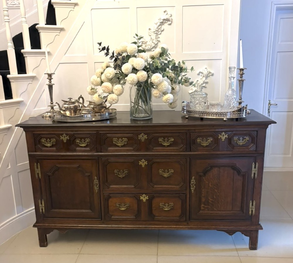 An antique dark oak Georgian dresser base featuring geometric panel drawers, brass handles, side cupboard doors, and a smooth wooden surface. View XIV