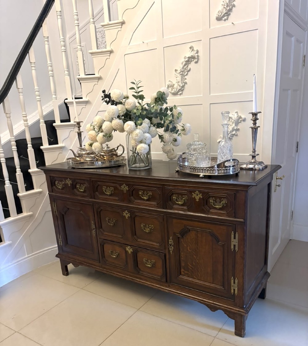 An antique dark oak Georgian dresser base featuring geometric panel drawers, brass handles, side cupboard doors, and a smooth wooden surface. View XV