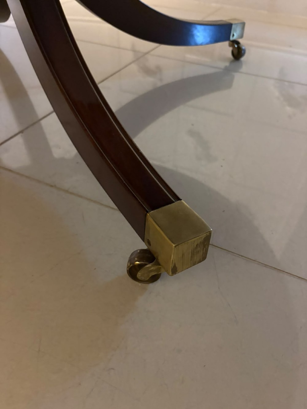 A circular mahogany dining table with a crossbanded edge tilted vertically on a central pedestal base with splayed legs and brass castors. View IV