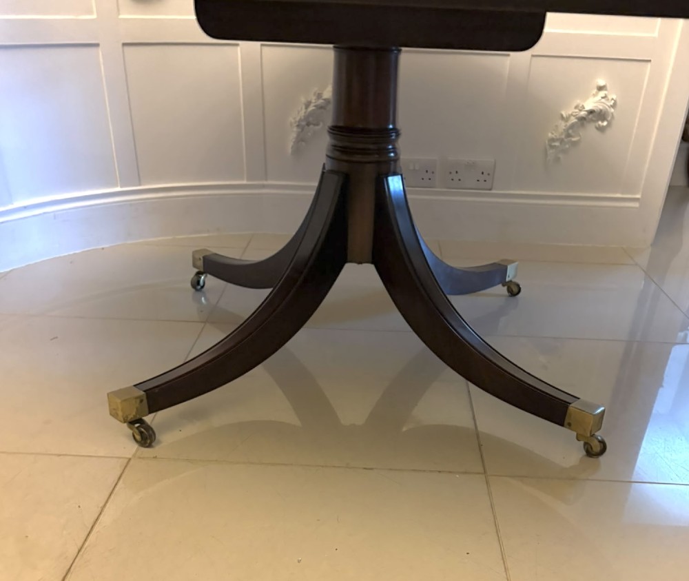 A circular mahogany dining table with a crossbanded edge tilted vertically on a central pedestal base with splayed legs and brass castors. View VIII