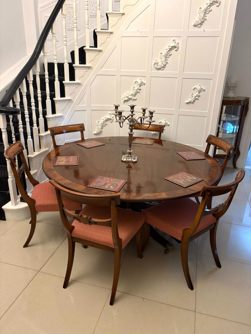 A circular mahogany dining table with a crossbanded edge tilted vertically on a central pedestal base with splayed legs and brass castors. View XI