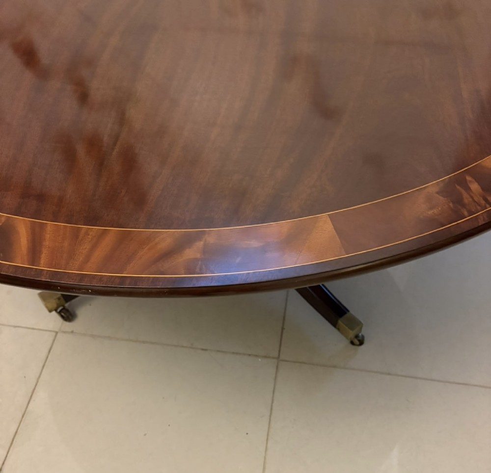 A circular mahogany dining table with a crossbanded edge tilted vertically on a central pedestal base with splayed legs and brass castors. View XII