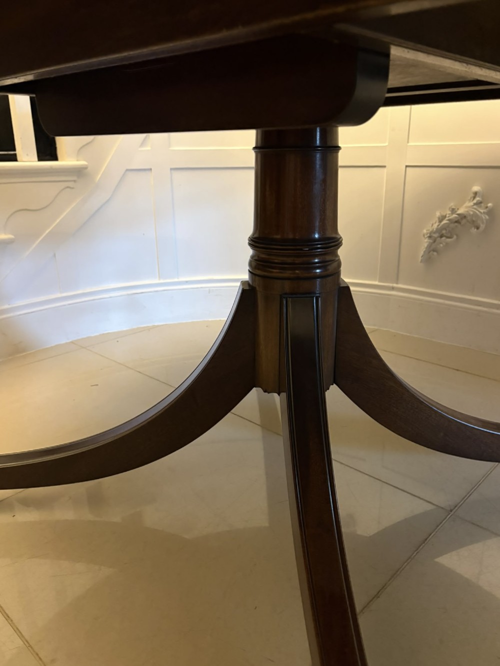 A circular mahogany dining table with a crossbanded edge tilted vertically on a central pedestal base with splayed legs and brass castors. View XIII