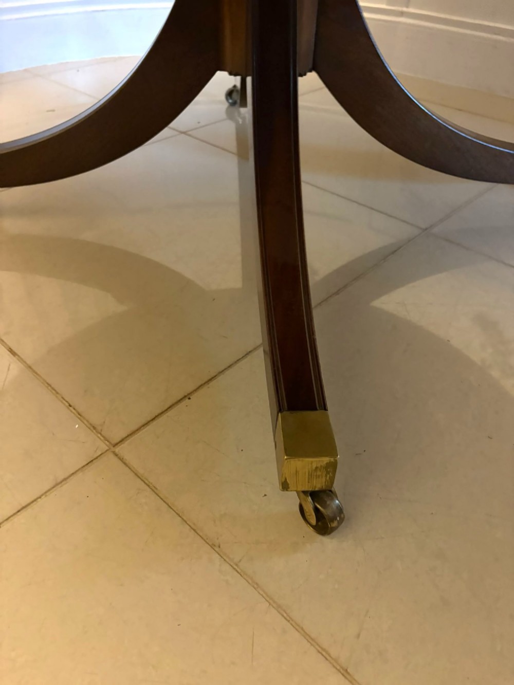 A circular mahogany dining table with a crossbanded edge tilted vertically on a central pedestal base with splayed legs and brass castors. View XIV