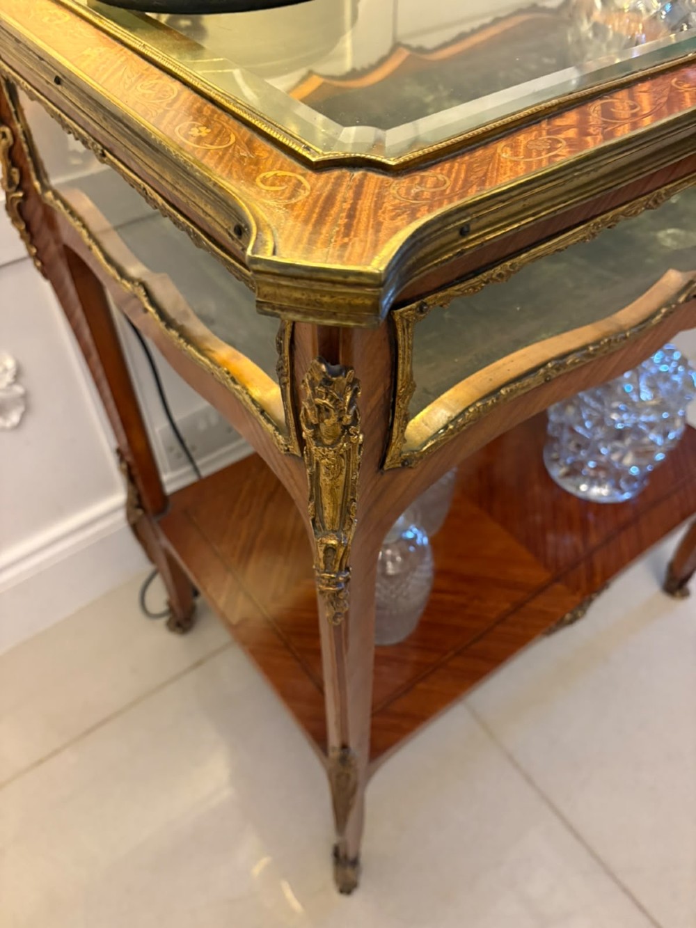 An antique French Napoleon III satinwood bijouterie table featuring a glazed display top, curved cabriole legs with decorative brass mounts, and an undertier shelf. View VII