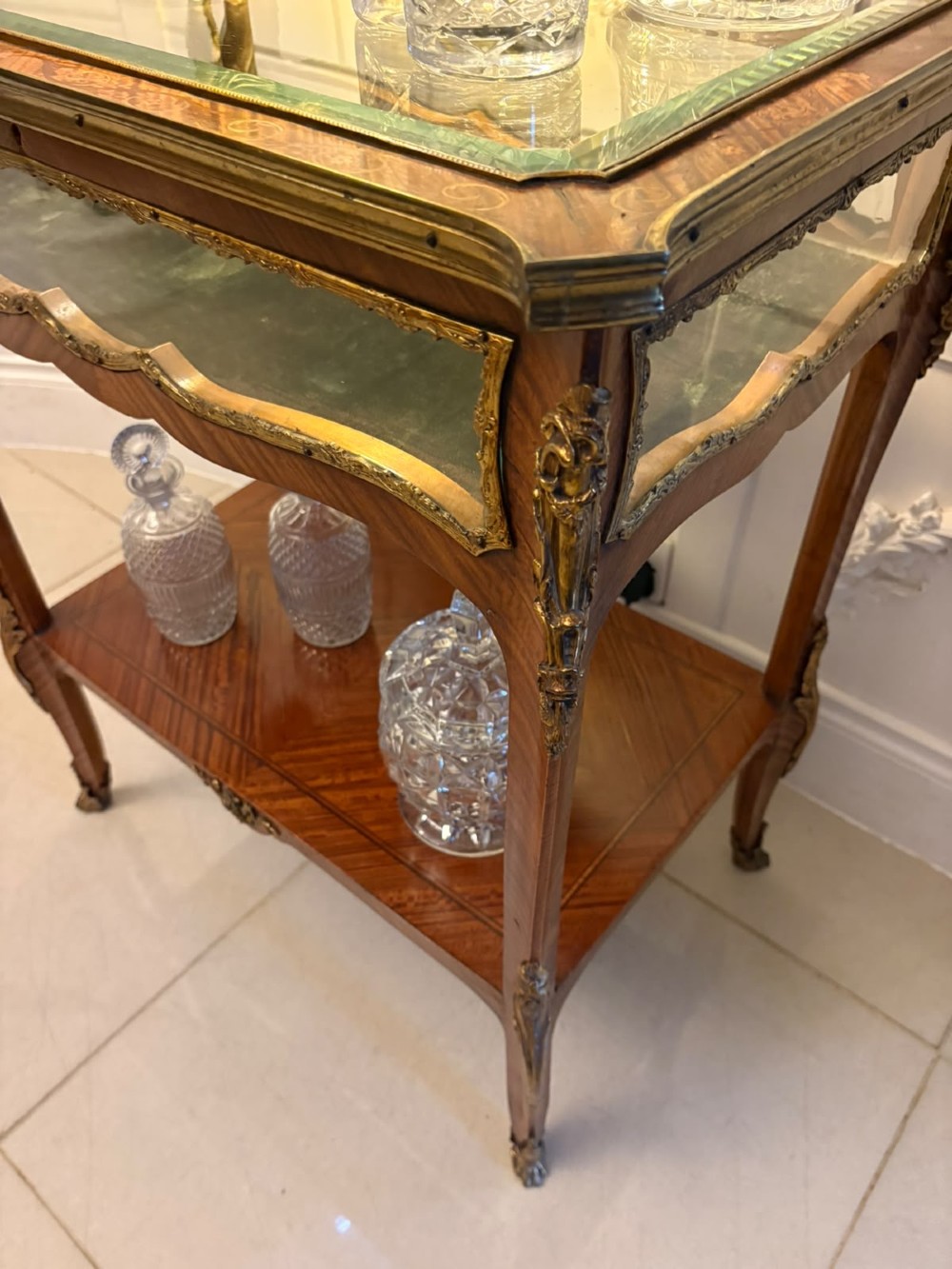 An antique French Napoleon III satinwood bijouterie table featuring a glazed display top, curved cabriole legs with decorative brass mounts, and an undertier shelf. View XI
