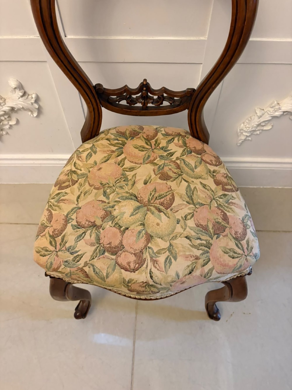 A set of four Victorian carved walnut dining chairs featuring open balloon backs, carved crest details, cabriole front legs, and floral pattern upholstered seats. View V