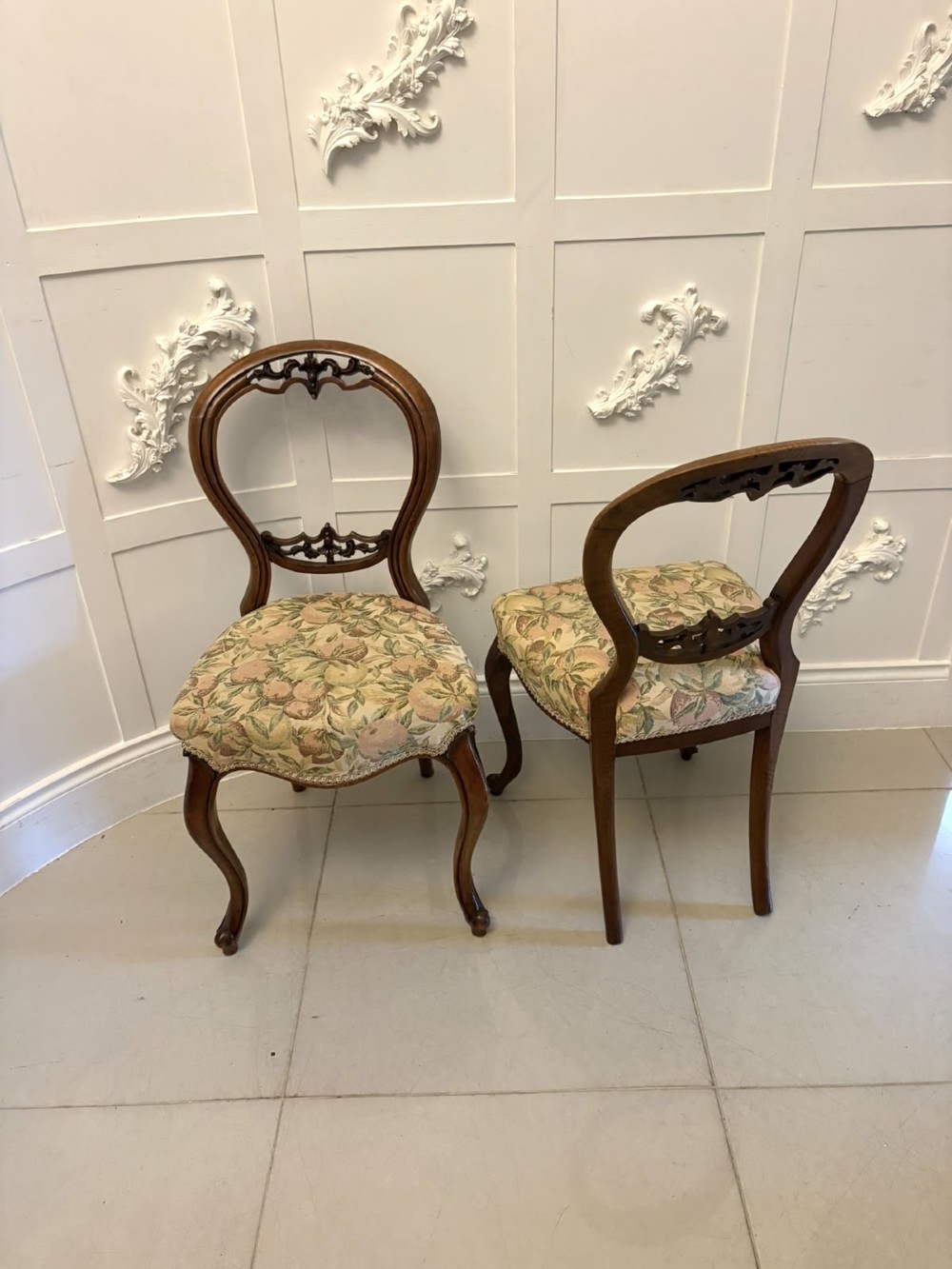 A set of four Victorian carved walnut dining chairs featuring open balloon backs, carved crest details, cabriole front legs, and floral pattern upholstered seats. View X
