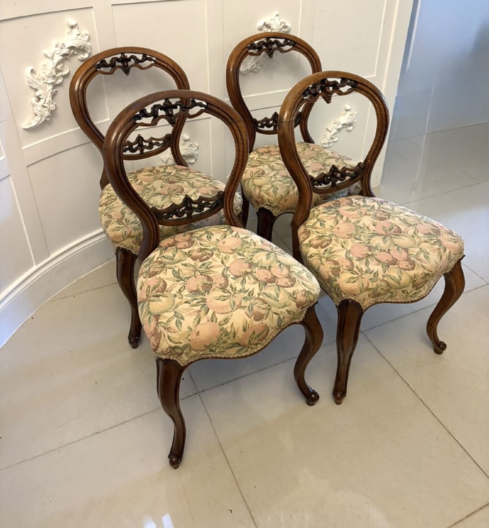 A set of four Victorian carved walnut dining chairs featuring open balloon backs, carved crest details, cabriole front legs, and floral pattern upholstered seats. View XI
