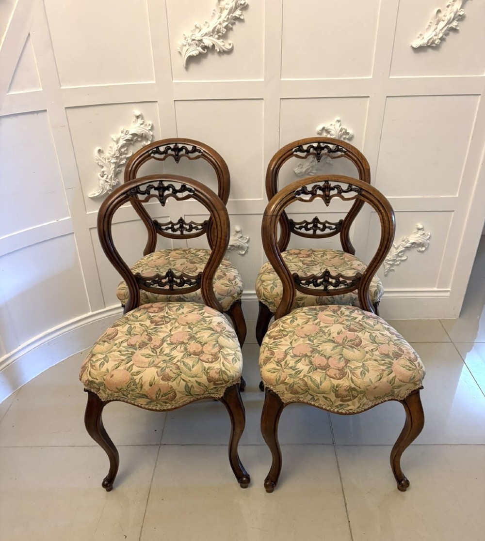 A set of four Victorian carved walnut dining chairs featuring open balloon backs, carved crest details, cabriole front legs, and floral pattern upholstered seats. View XII