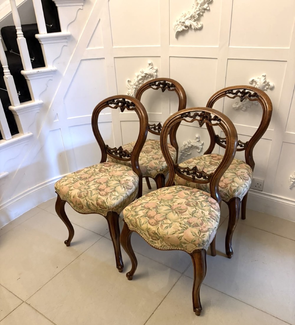 A set of four Victorian carved walnut dining chairs featuring open balloon backs, carved crest details, cabriole front legs, and floral pattern upholstered seats.