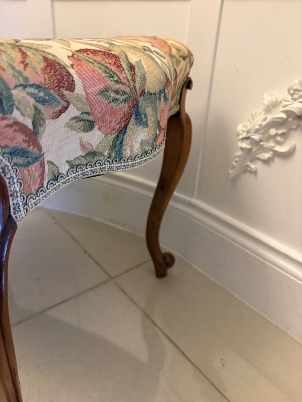 A low rectangular Victorian footstool featuring carved walnut cabriole legs and a padded seat upholstered in a botanical tapestry fabric depicting fruit and foliage. View IV
