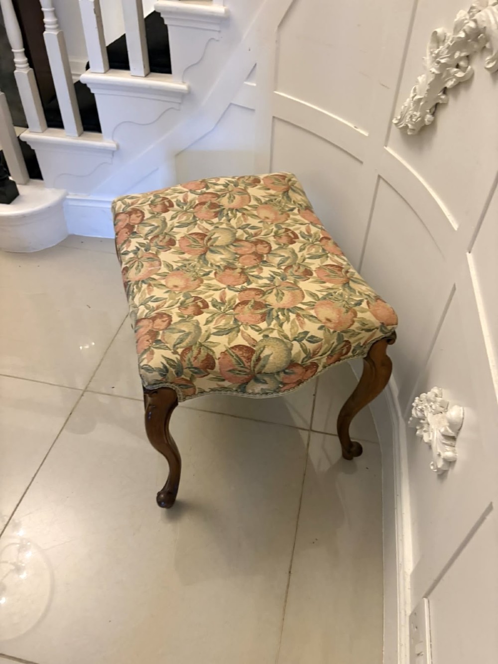 A low rectangular Victorian footstool featuring carved walnut cabriole legs and a padded seat upholstered in a botanical tapestry fabric depicting fruit and foliage. View VI