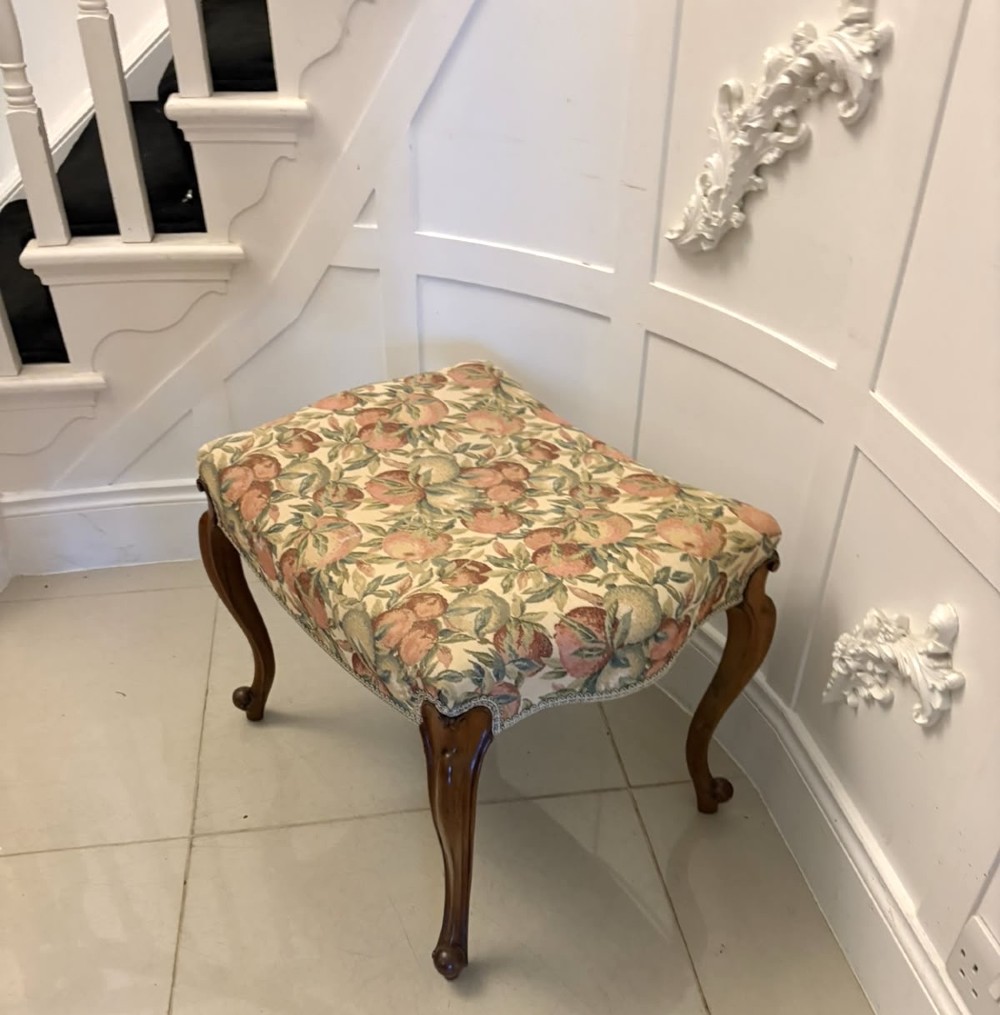 A low rectangular Victorian footstool featuring carved walnut cabriole legs and a padded seat upholstered in a botanical tapestry fabric depicting fruit and foliage. View XI