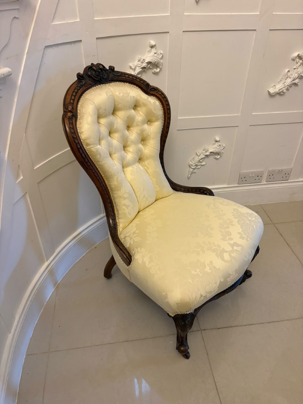 A Victorian carved walnut slipper chair featuring a button-tufted cream damask spoon-shaped backrest and cabriole front legs.