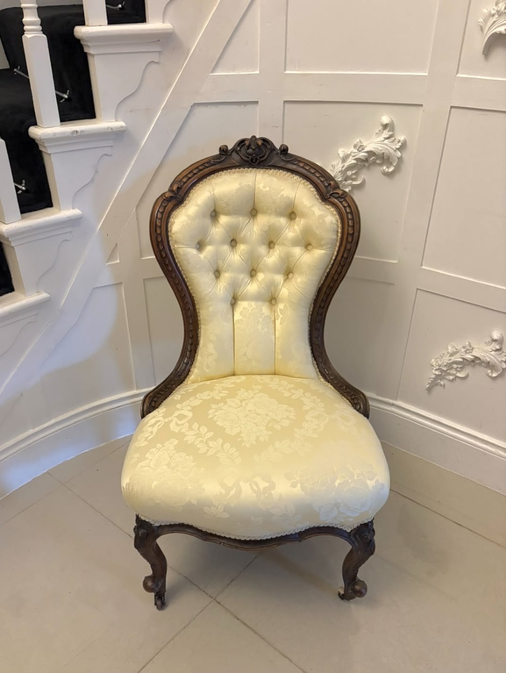 A Victorian carved walnut slipper chair featuring a button-tufted cream damask spoon-shaped backrest and cabriole front legs. View VII