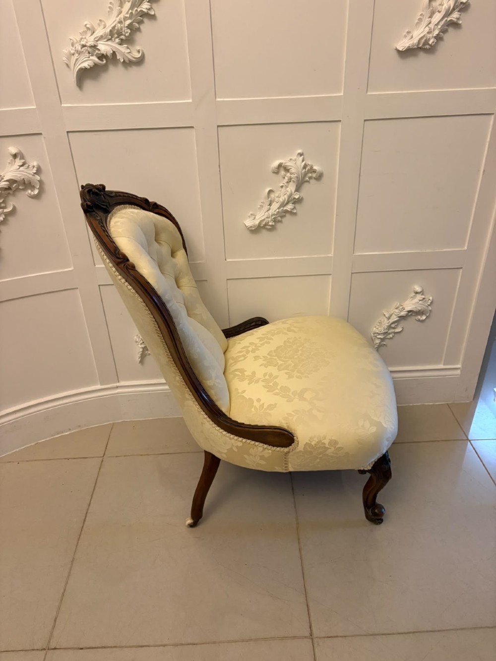 A Victorian carved walnut slipper chair featuring a button-tufted cream damask spoon-shaped backrest and cabriole front legs. View XIV