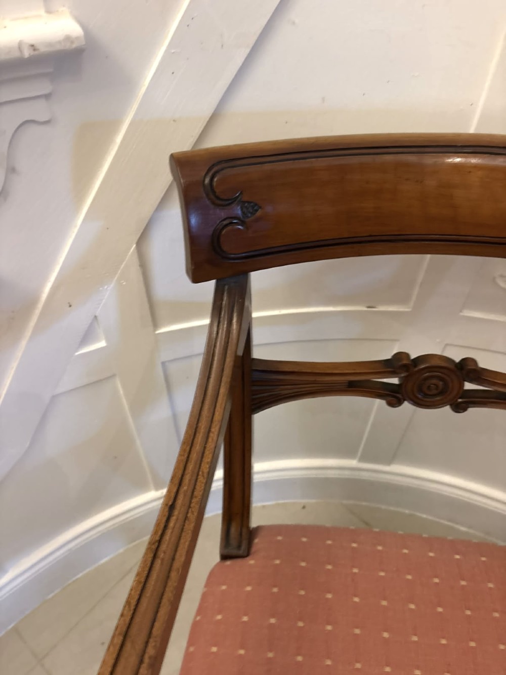 An antique mahogany carver dining chair with sweeping armrests, a carved central roundel crest bar, and a pink patterned upholstered seat. View VI