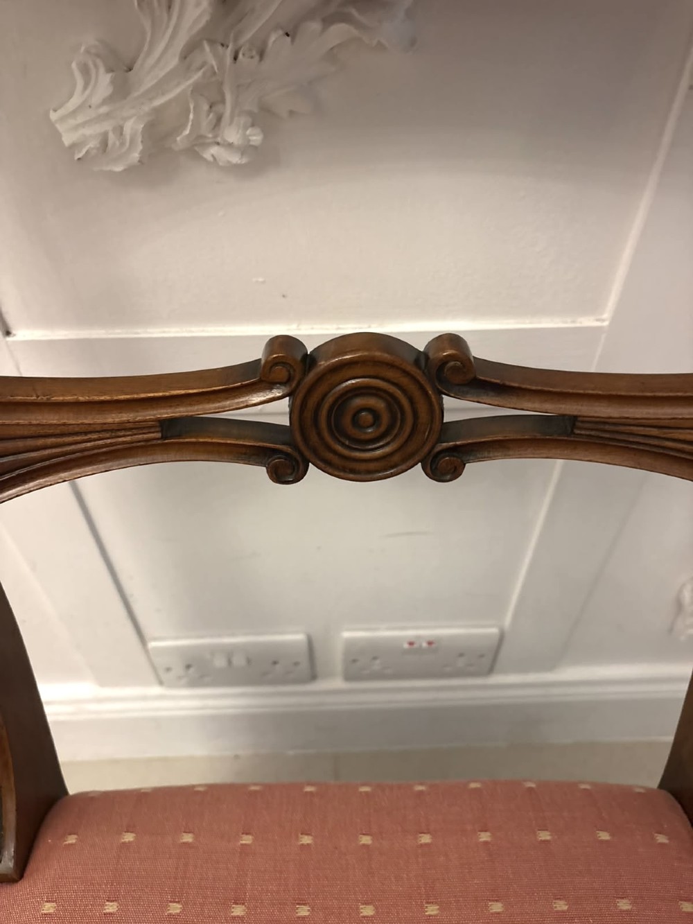 An antique mahogany carver dining chair with sweeping armrests, a carved central roundel crest bar, and a pink patterned upholstered seat. View XIV